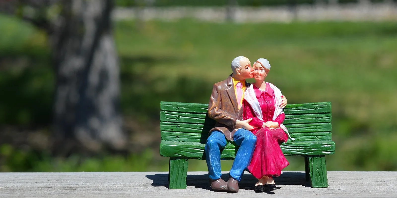 An older couple sitting together on a green park bench