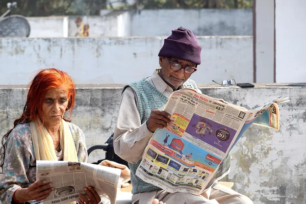 An older man and a woman sitting side by side reading newspapers