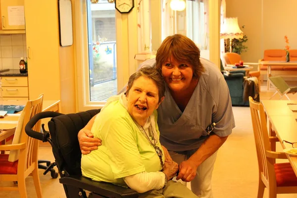A caregiver smiling with an older woman in a wheelchair in a bright care home