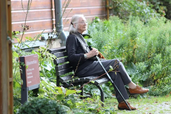 An older man sitting on a bench in a leafy garden