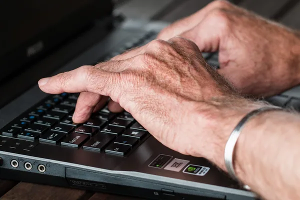 Close-up of an older person's hands typing on a laptop keyboard
