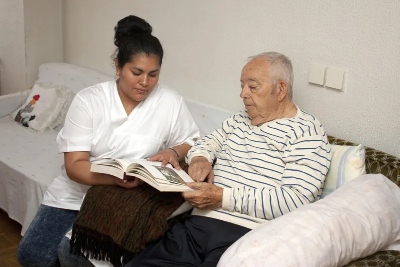 A caregiver and an older man reading together