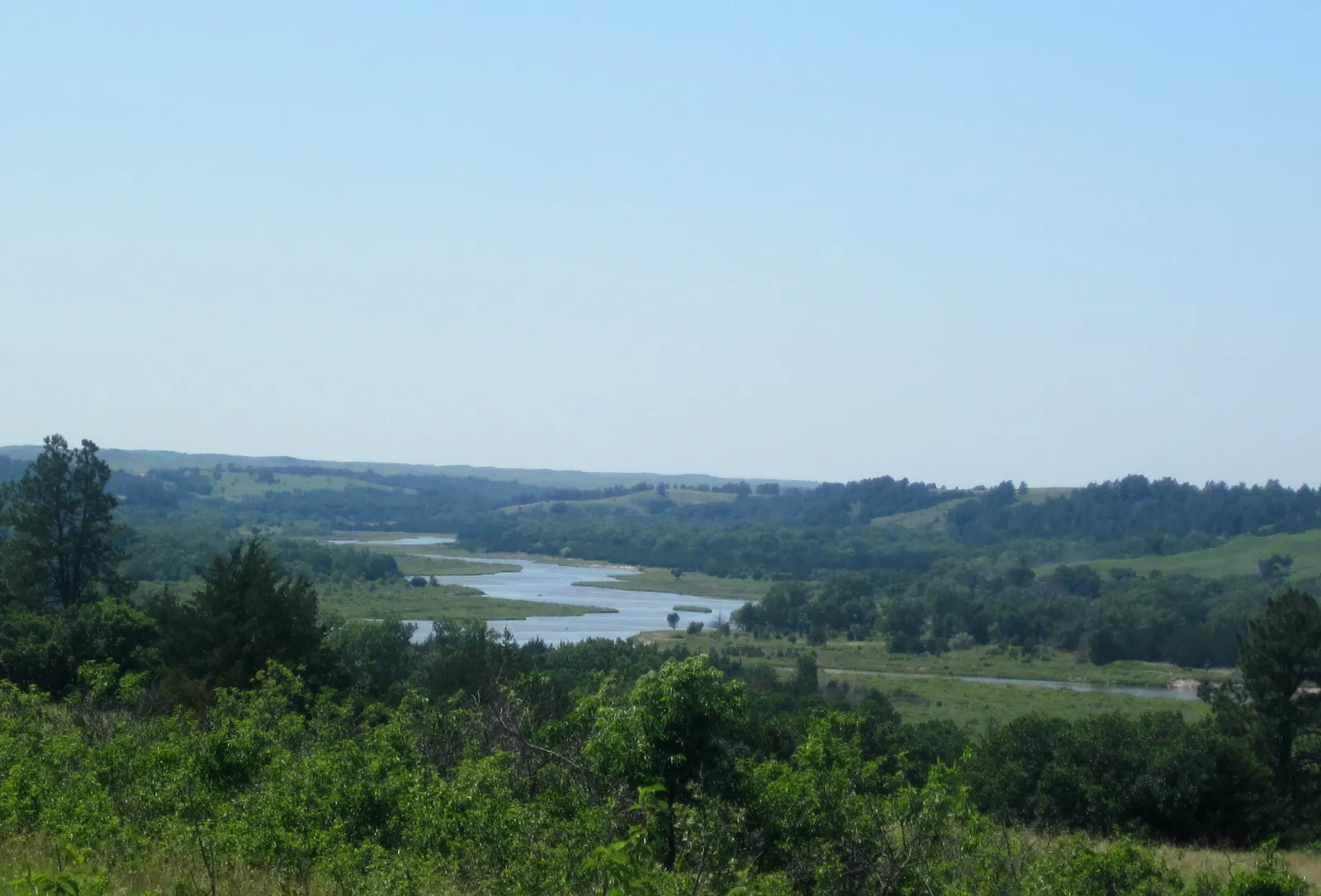 View of a long, winding river under a light blue sky. The middle section of the Niobrara NSR is more open than the upper section, with fewer bluffs along...